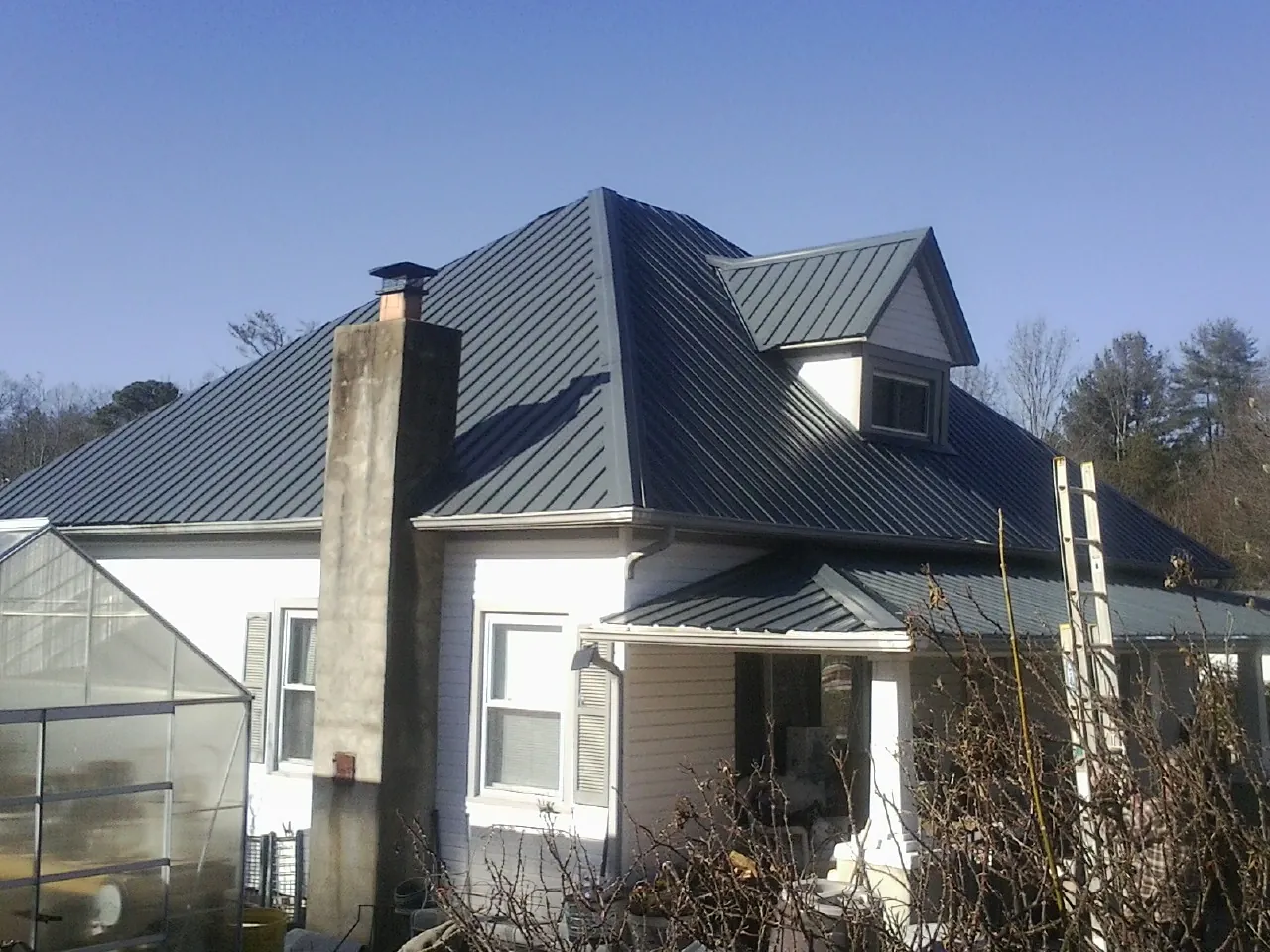 Dark blue standing seam metal roof on a white farmhouse with dormer — Slate & Tile Roof Repair by Roofing Brothers in Mc Cracken