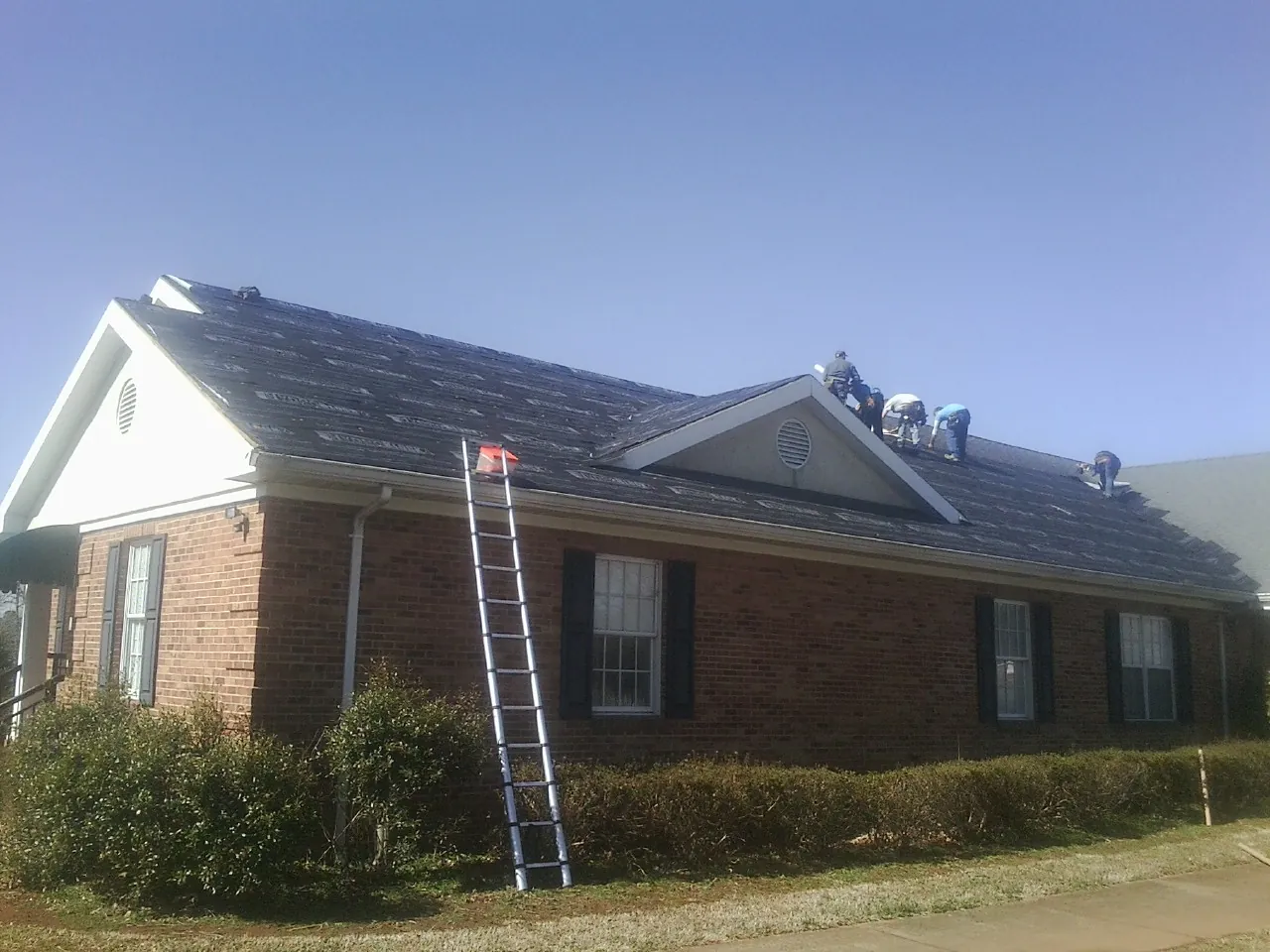 Crew tearing shingles off a brick ranch roof with a ladder set — Emergency Roof Repair work by our crew in Mc Cracken