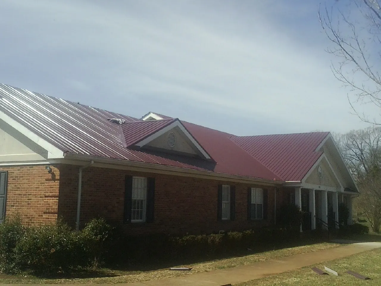 Red metal roof with gabled entries on a long brick building, from a Hail Damage Roof Repair job in Mc Cracken