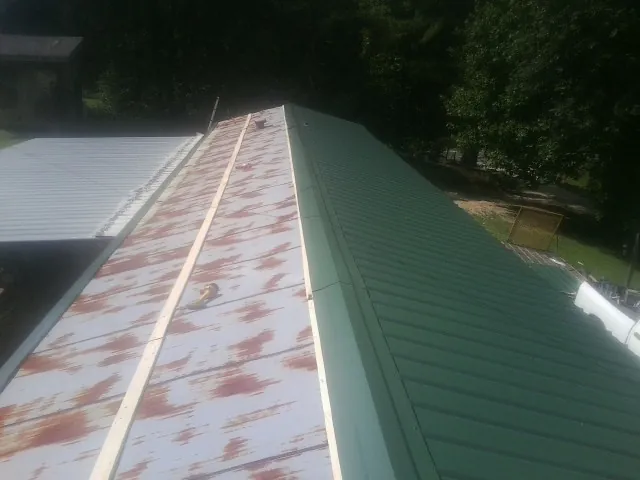 Old rusted panels beside newly installed green metal roofing — Wind Damage Roof Repair by Roofing Brothers in Mc Cracken