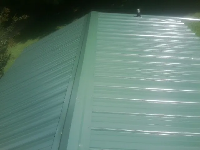 New green metal panels meeting at the ridge of a roof — Flat Roof Repair work by our crew in Mc Cracken