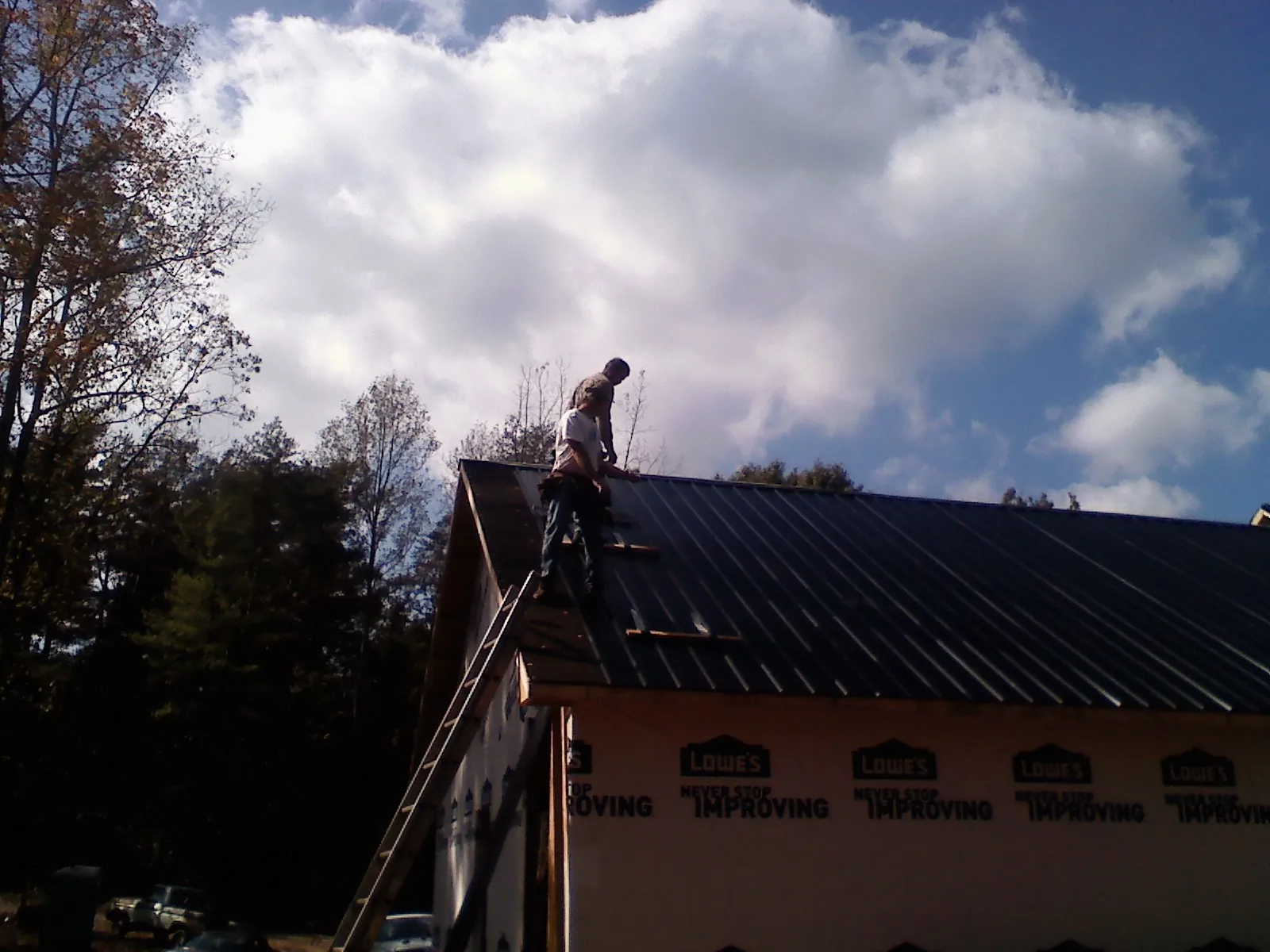 Roofer fastening dark metal panels high against a cloudy sky, from a Roof Inspection job in Mc Cracken