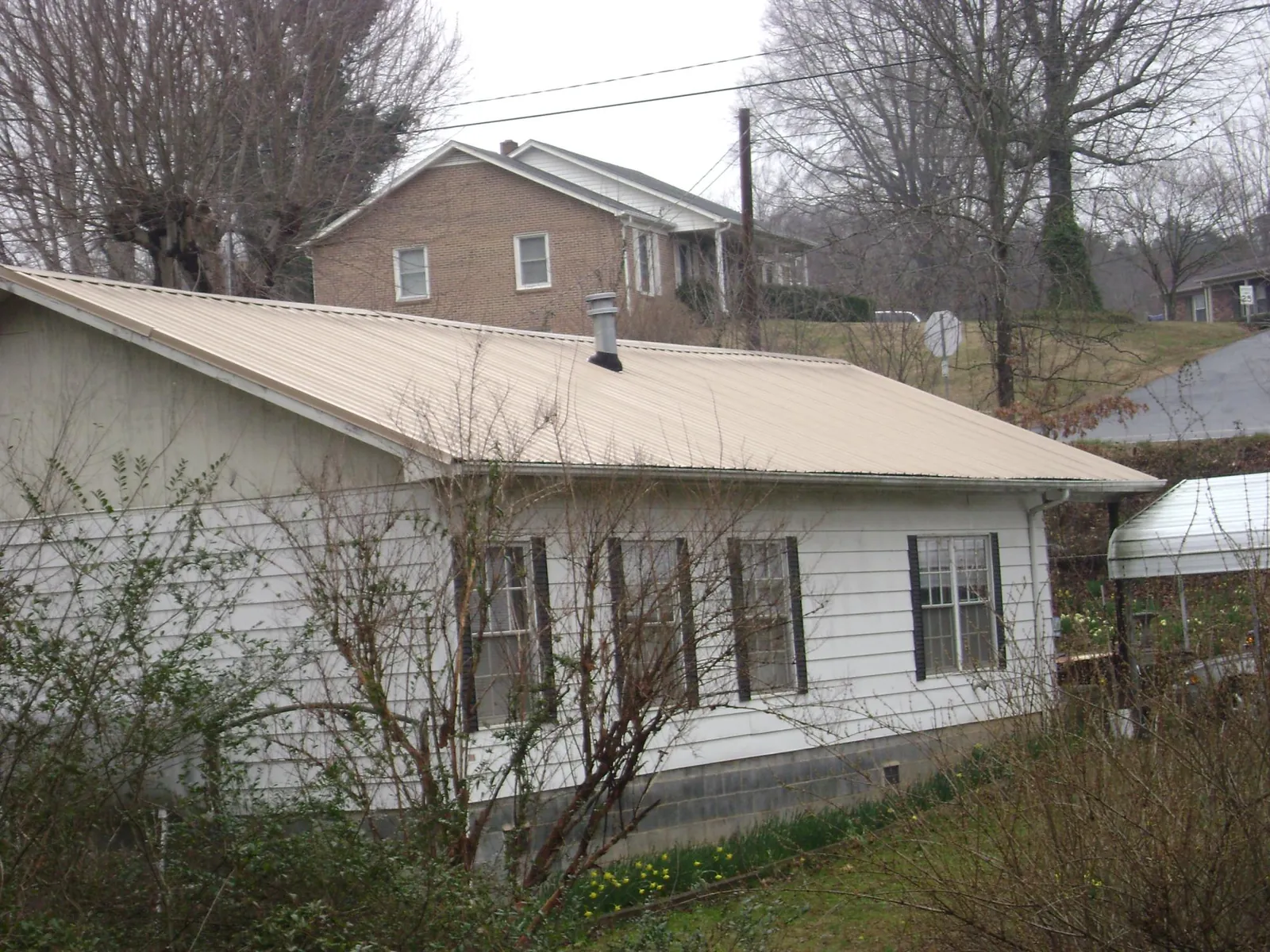 Tan metal roof on a white sided house set into a hillside — Commercial Roofing by Roofing Brothers in Mc Cracken