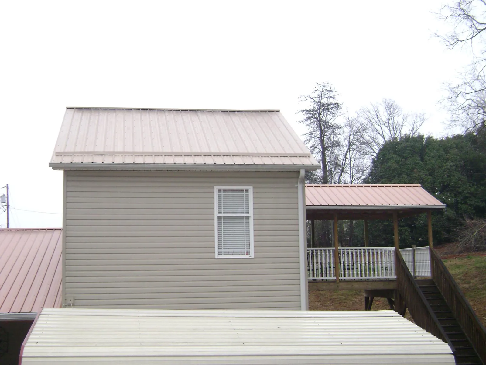 Tan metal roofs on a two story addition and attached porch, from a Roof Replacement job in Mc Cracken